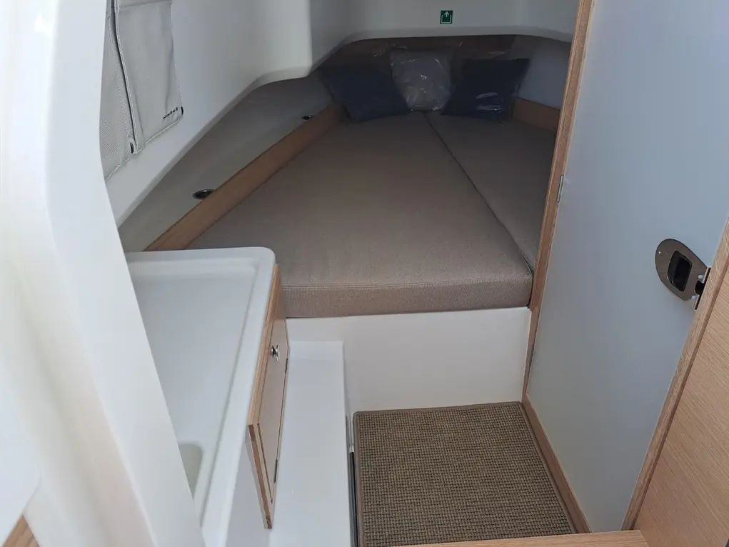 Interior of a boat cabin featuring a double berth, drawer storage, and light-colored wood finishes; two pillows on the bed.